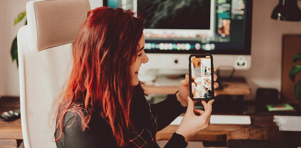 Woman showing a mobile website on her phone, in front of a computer screen.