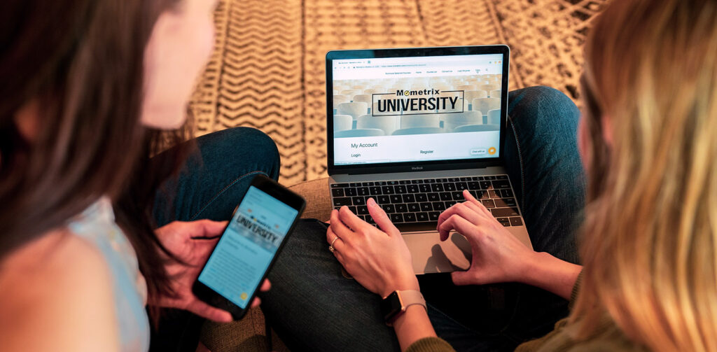 One person looking at a website on her laptop and another sitting next to her with her cellphone on the same webpage