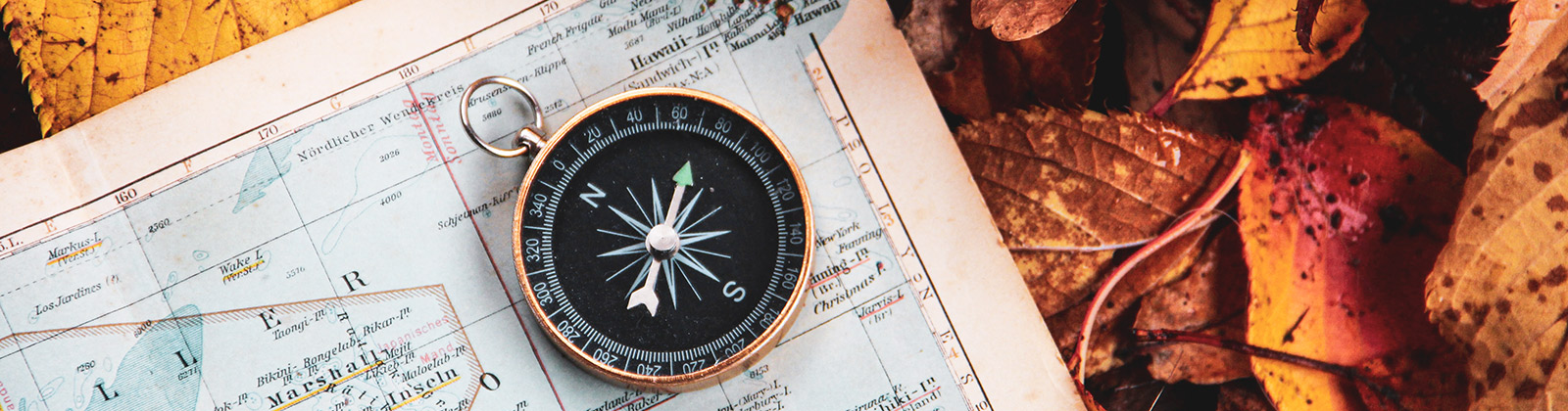 Compass laying on a map with fall leaves in the background
