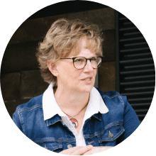 Elaine Klemmensen, wearing glasses, a denim jacket over white-collared shirt, is talking to someone
