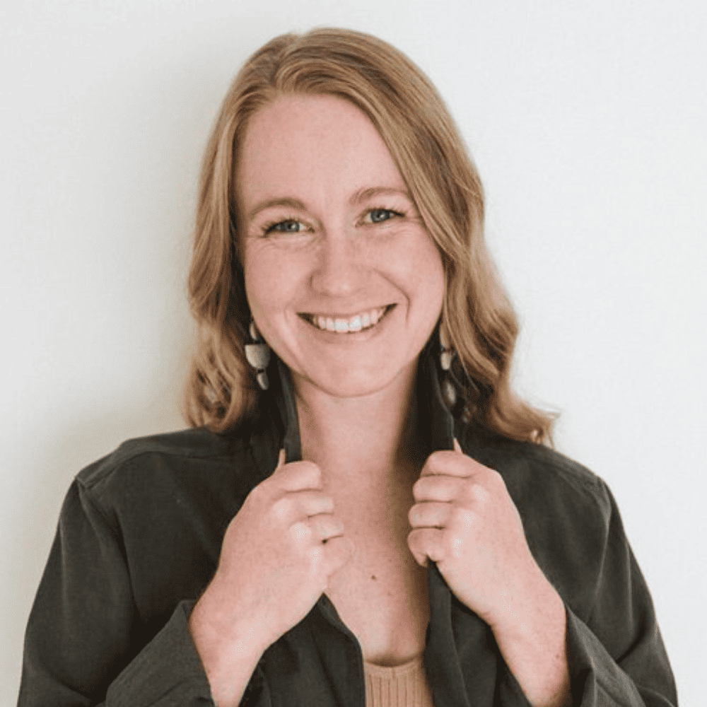 Sydney Fletcher is holding the collar of her green jacket and smiling widely at the camera